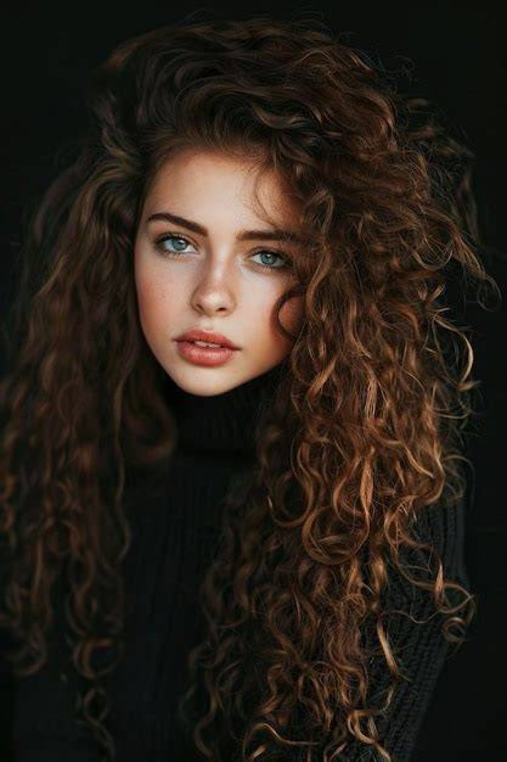 a woman with long curly hair wearing a black dress and smiling at the